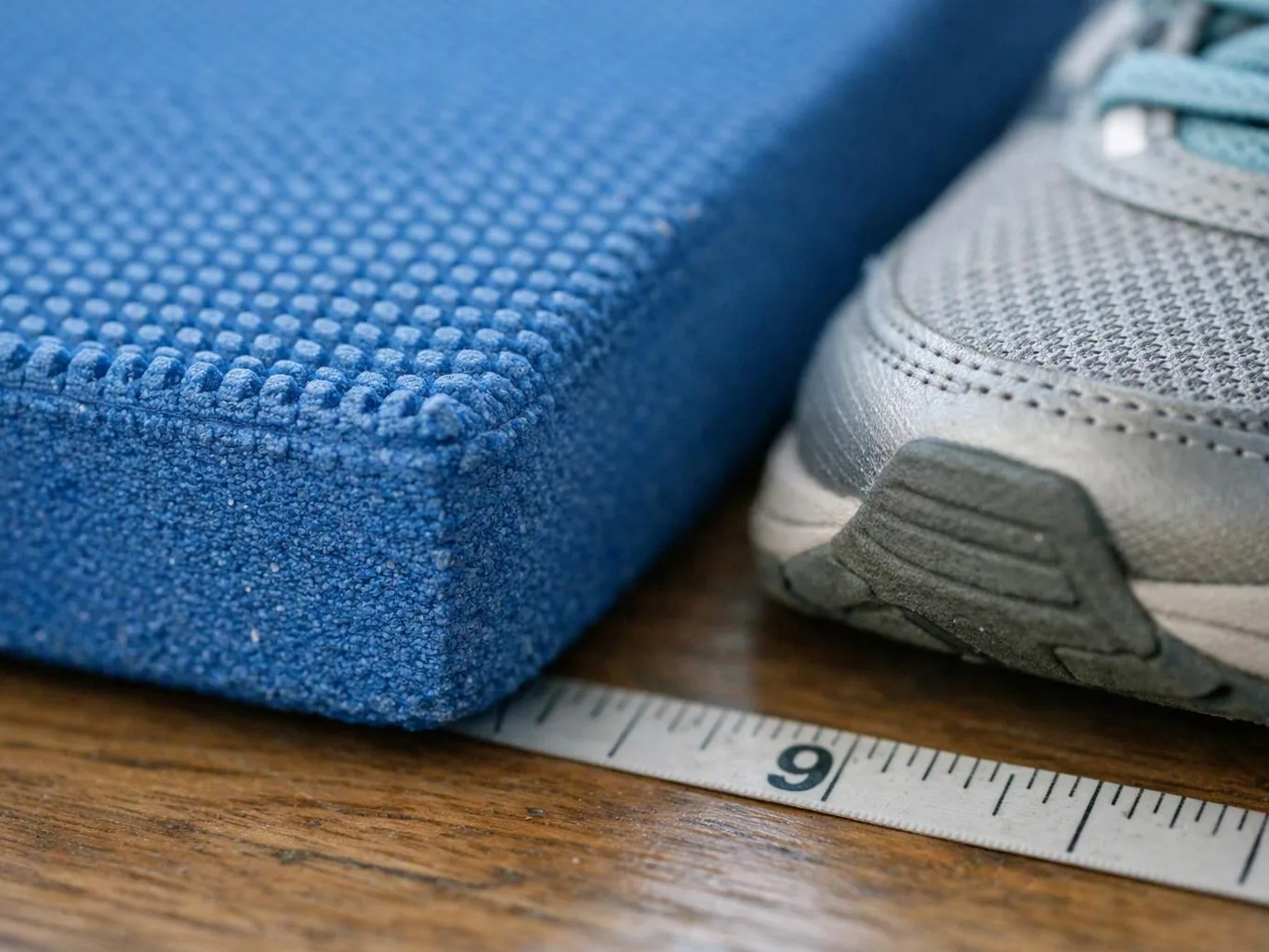 A blue foam block and a gray sneaker rest beside a measuring tape on a wooden surface