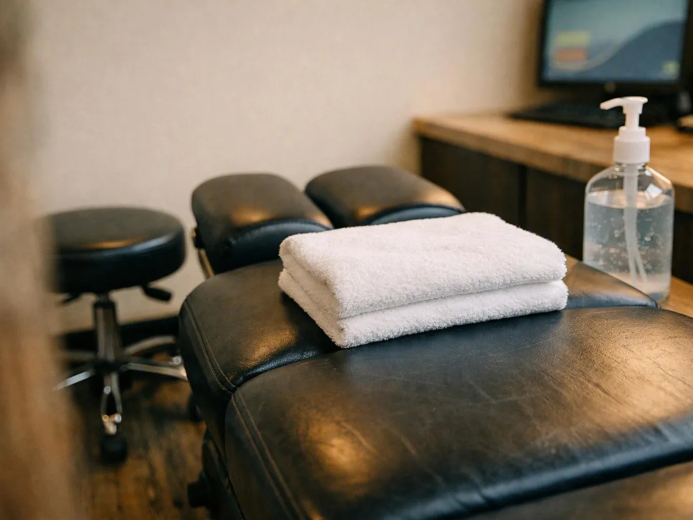 Folded white towels rest on a black treatment table beside a sanitizer bottle and stool
