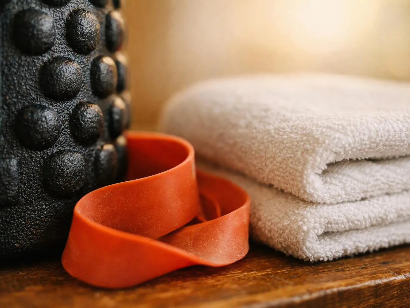 An orange resistance band lies beside folded white towels and a textured black foam roller on wood